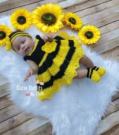 a baby wearing a bee outfit laying on a white rug with sunflowers in the background