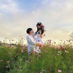 a man and woman standing in the middle of a field with pink flowers on it