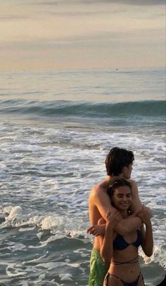 two people standing in the ocean hugging each other