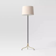 a floor lamp with a white shade on the base and a black metal pole,