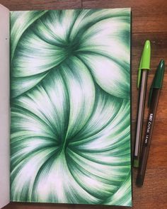 an open notebook with green and white swirls on it, next to two markers