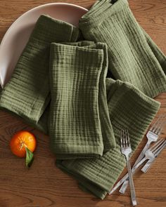 a white plate topped with green napkins next to an orange on top of a wooden table