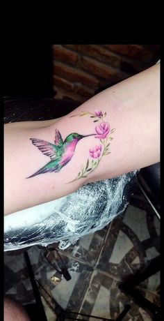 a hummingbird with pink flowers on it's left arm and the back of its leg