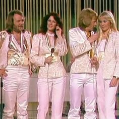 four women in white outfits standing next to each other and one man is talking on the phone