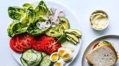 a white plate topped with sliced up tomatoes and cucumbers next to a bowl of mayonnaise