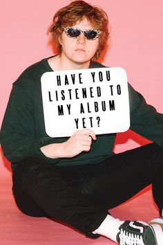 a man sitting on the ground holding a sign that says have you listened to my album yet?