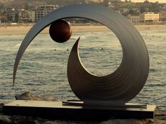 a sculpture on the beach with people swimming in the water