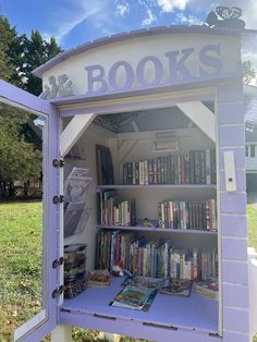 a purple and white book stand with books on it's shelves in the grass