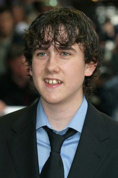 a young man in a suit and tie smiling for the camera with people behind him