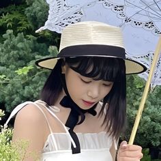 a woman wearing a white dress and black hat holding an umbrella in her hand while standing next to some bushes