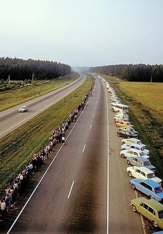 a long line of cars parked on the side of a road next to an open field