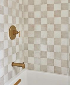 a bath tub sitting under a faucet next to a tiled wall