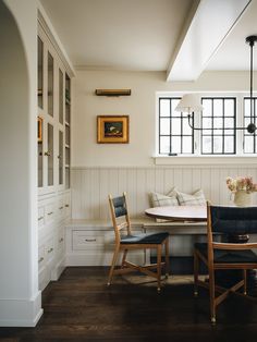 a dining room table with two chairs and a bench in front of the window, next to a built - in bookshelf