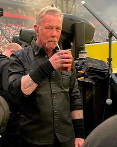 a man in black shirt drinking from a cup next to a microphone at a football game