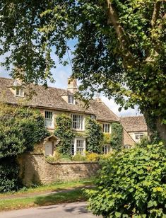 an old stone house with ivy growing on it's walls and trees in the foreground