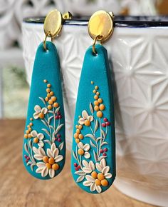 two pairs of blue earrings with flowers painted on them sitting in front of a cup