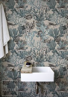 a bathroom sink sitting under a mirror next to a wallpaper covered in seaweed