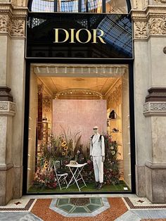 a man standing in front of a dior store window with flowers and chairs on display