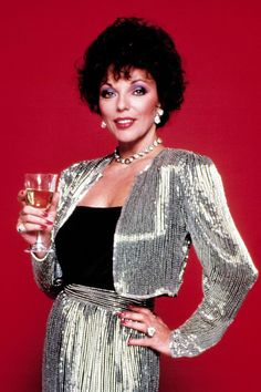 a woman holding a glass of wine in her right hand and wearing a gold jacket