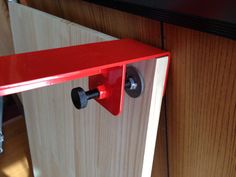 a red door handle is attached to the side of a wood paneled wall with two screws