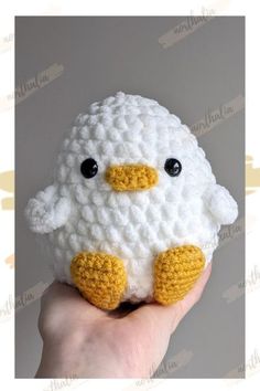 a hand holding a small white crocheted stuffed animal with black eyes and yellow beak