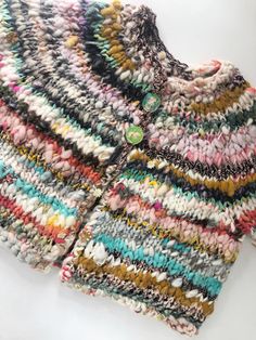 a multicolored knitted jacket with buttons on the front and back, sitting on a white surface