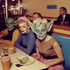 three people sitting at a table with masks on their faces and food in front of them