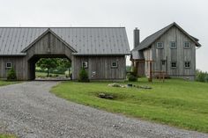 an old barn sits in the middle of a grassy field with a gravel road leading to it