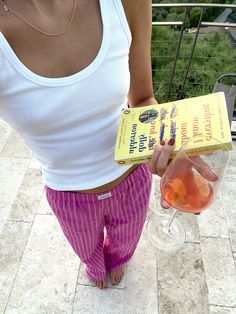 a woman holding a book and a wine glass in her hand while standing on a patio