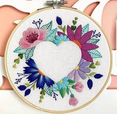 a heart - shaped frame with flowers and leaves is hanging on a wall in front of a pink background