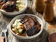 two white bowls filled with meat and mashed potatoes on top of a wooden table