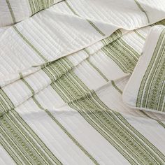 an unmade bed with green and white striped comforter on it's side