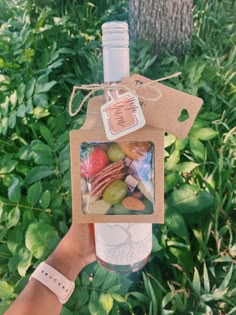 a person holding up a wine bottle with some fruit on it in front of trees