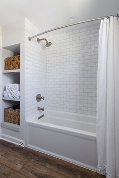 a bathroom with white tile and wooden floors, including a shower curtain over the bathtub