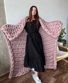 a woman standing in front of a giant knitted chair with her arms wrapped around it