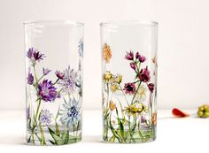 two glass vases with colorful flowers painted on the side and one filled with water