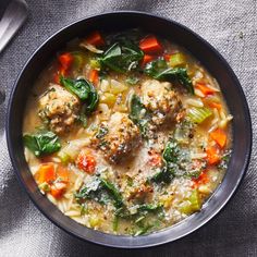 a bowl of soup with meatballs, carrots and spinach