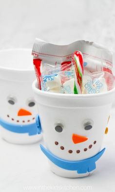 two cups filled with candy and marshmallows in the shape of snowmen