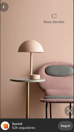 a pink chair next to a table with a lamp on it and a white wall behind it