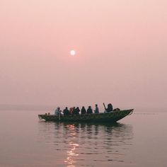 a group of people in a small boat on the water at sunset or sunrise time