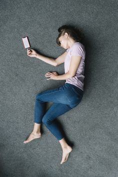 a woman laying on the floor with her cell phone in her hand and looking down