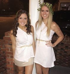 two beautiful young women standing next to each other near a white pole in front of a brick wall