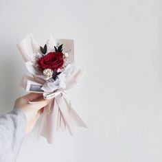 someone is holding a red rose and white ribbon bouquet in their left hand, on a white background