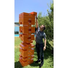 a man standing next to a tall stack of orange boxes on top of green grass