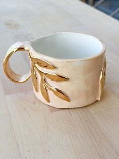 a white ceramic cup with gold leaves on it