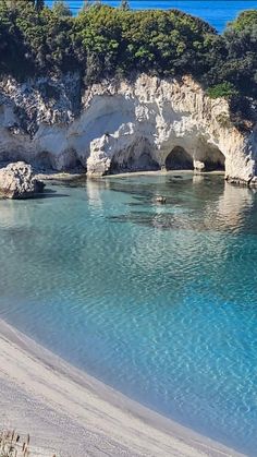 the water is crystal blue and there are people swimming in it on the beach near some cliffs