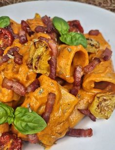 a white plate topped with pasta covered in cheese and bacon next to green leafy greens