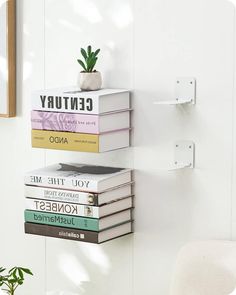 a stack of books sitting on top of a white wall next to a chair and potted plant