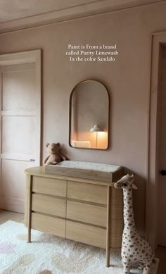 a baby's room with pink walls and a wooden dresser in front of a mirror