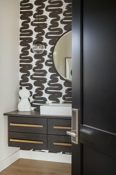 a bathroom with black and white wallpaper, wooden drawers and a mirror on the door